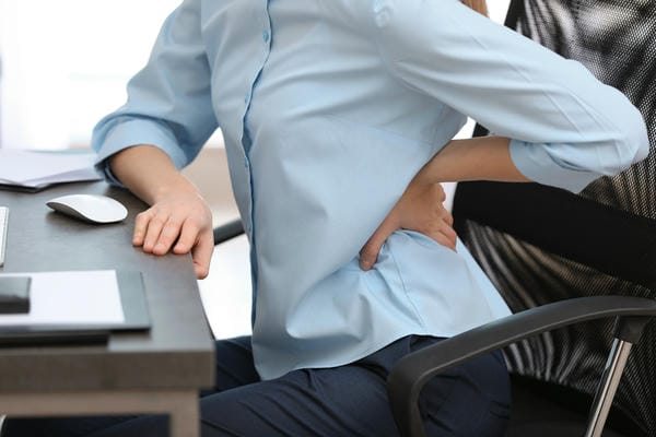 Arbeitsbedingungen mit Rheuma Frau hält sich wegen Rückenschmerzen den Rücken, am Schreibtisch