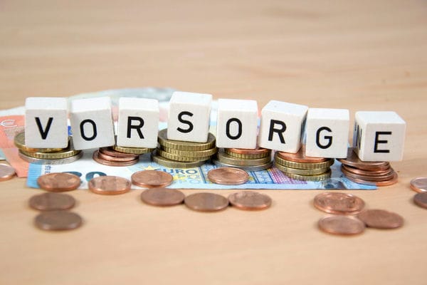 altersleben-altersvorsorge Kleine Würfel mit Buchstaben, welche Altersvorsorge bilden, liegen auf einen Haufen Geld.