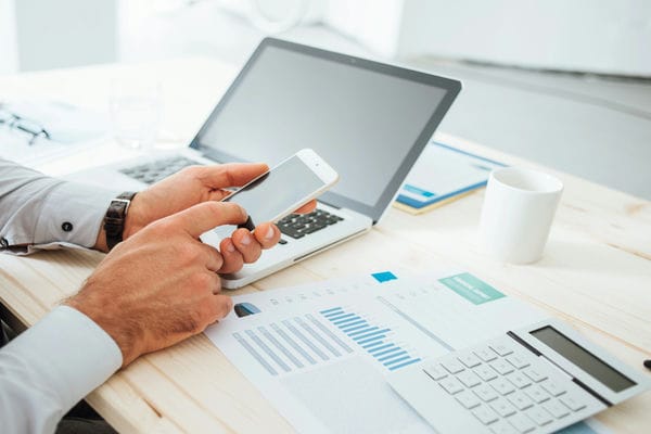 arbeitsleben-diensthandy-homeoffice Geschäftsmann arbeitet am Bürotisch mit einem Diensthandy im Homeoffice