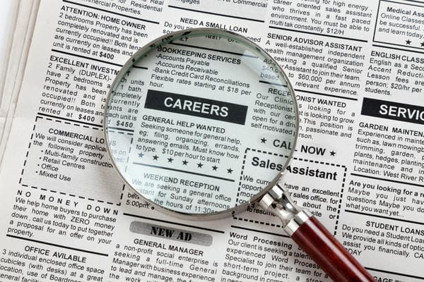 bewerbung-stellenanzeige Eine Lupe vergrößert das Wort „CAREERS“ inmitten verschiedener Stellenanzeigen in einer gedruckten Zeitung.