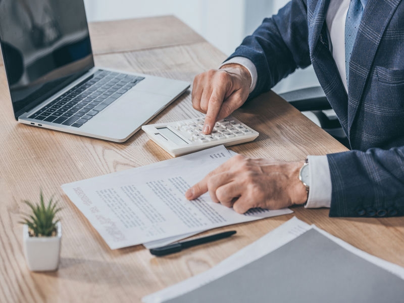 Die Abfindung ist eine Entschädigung für die Beendigung des Arbeitsverhältnisses. Geschäftsmann, der am Tisch sitzt, Dokument liest und mit Taschenrechner im Büro zählt