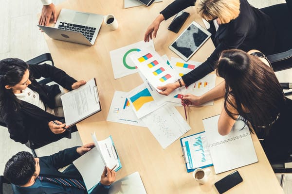 unternehmen-arbeitsgemeinschaft Eine Arbeitsgemeinschaft sitzt an einem Tisch und analysiert gemeinsam verschiedene Diagramme und Dokumente während einer Besprechung aus der Vogelperspektive.