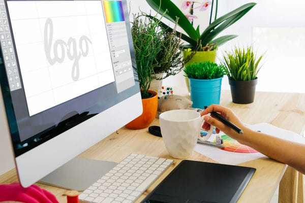unternehmen-firmenlogo Schreibtisch mit Computer, auf dem ein Mensch ein neues Logo mit einem Tablet erstellt