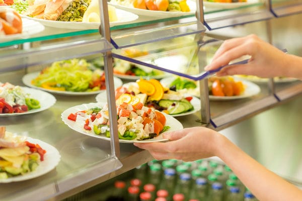 unternehmen-gemeinschaftsverpflegung Ein Mitarbeiter bedient sich an der Gemeinschaftsverpflegung und nimmt sich einen Teller Salat.